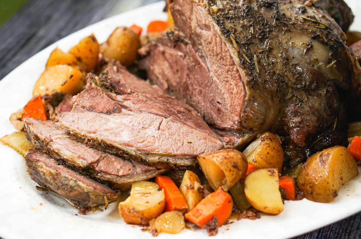 closeup of a crock pot lab roast surrounded by roasted vegetables on a white platter