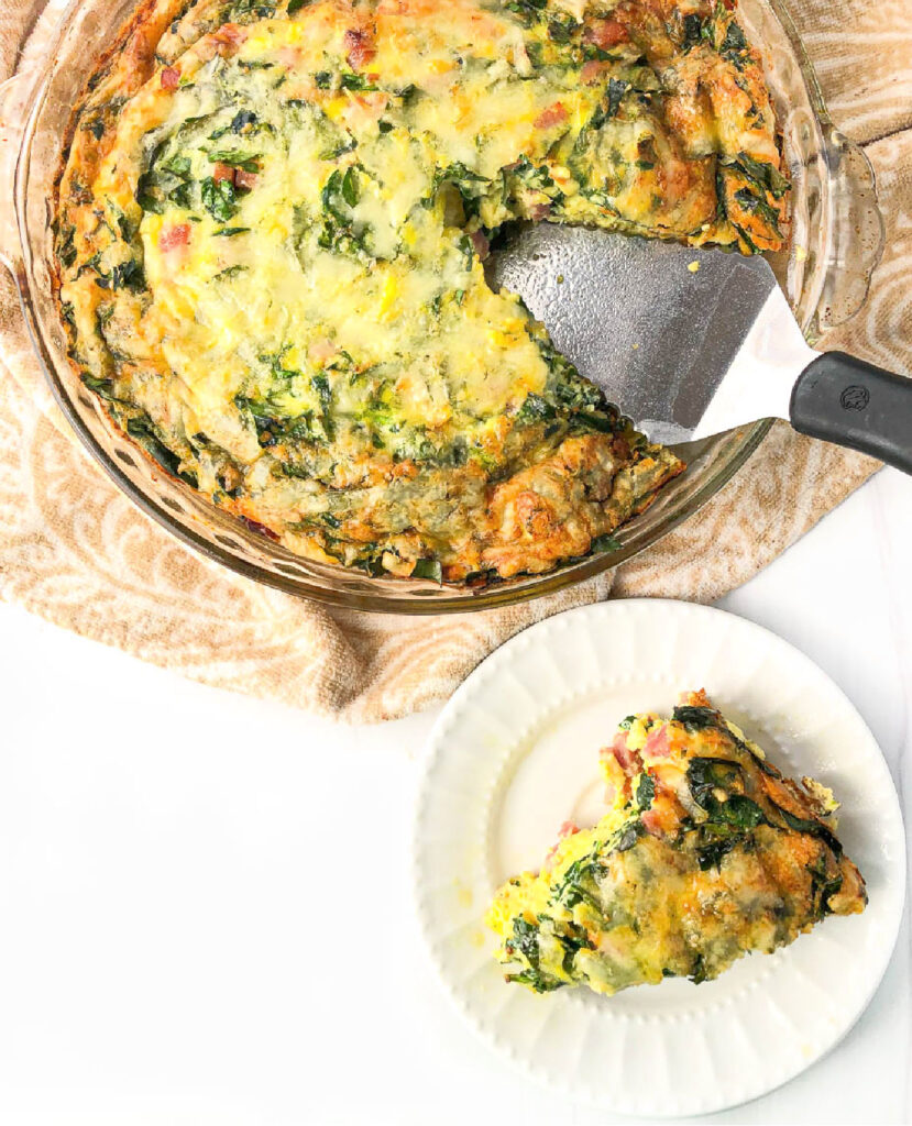 Aerial view of a pie pan with low carb ham and spinach quiche with a white plate with a slice.