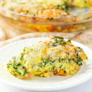 Closeup of a piece of keto quiche recipe with spinach, ham and cheese on a white plate.