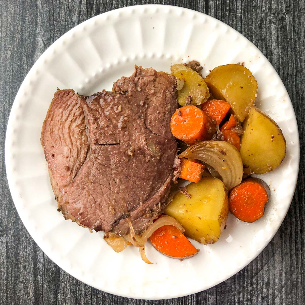 white plate with a slice of lamb and roasted potatoes and carrots