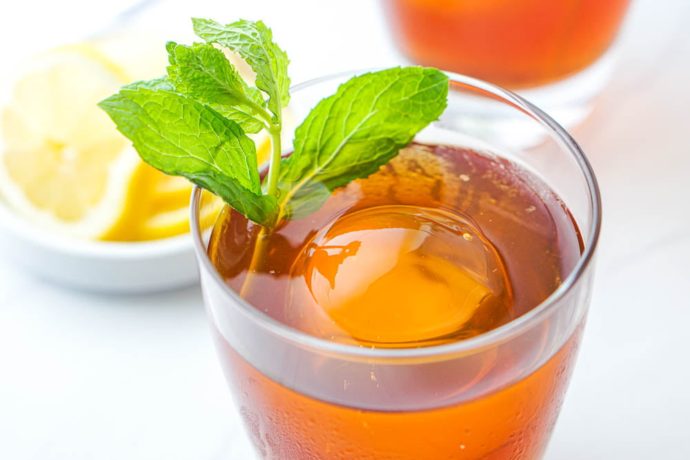 closeup of a cocktail glass with large round ice cube and sprig of mint