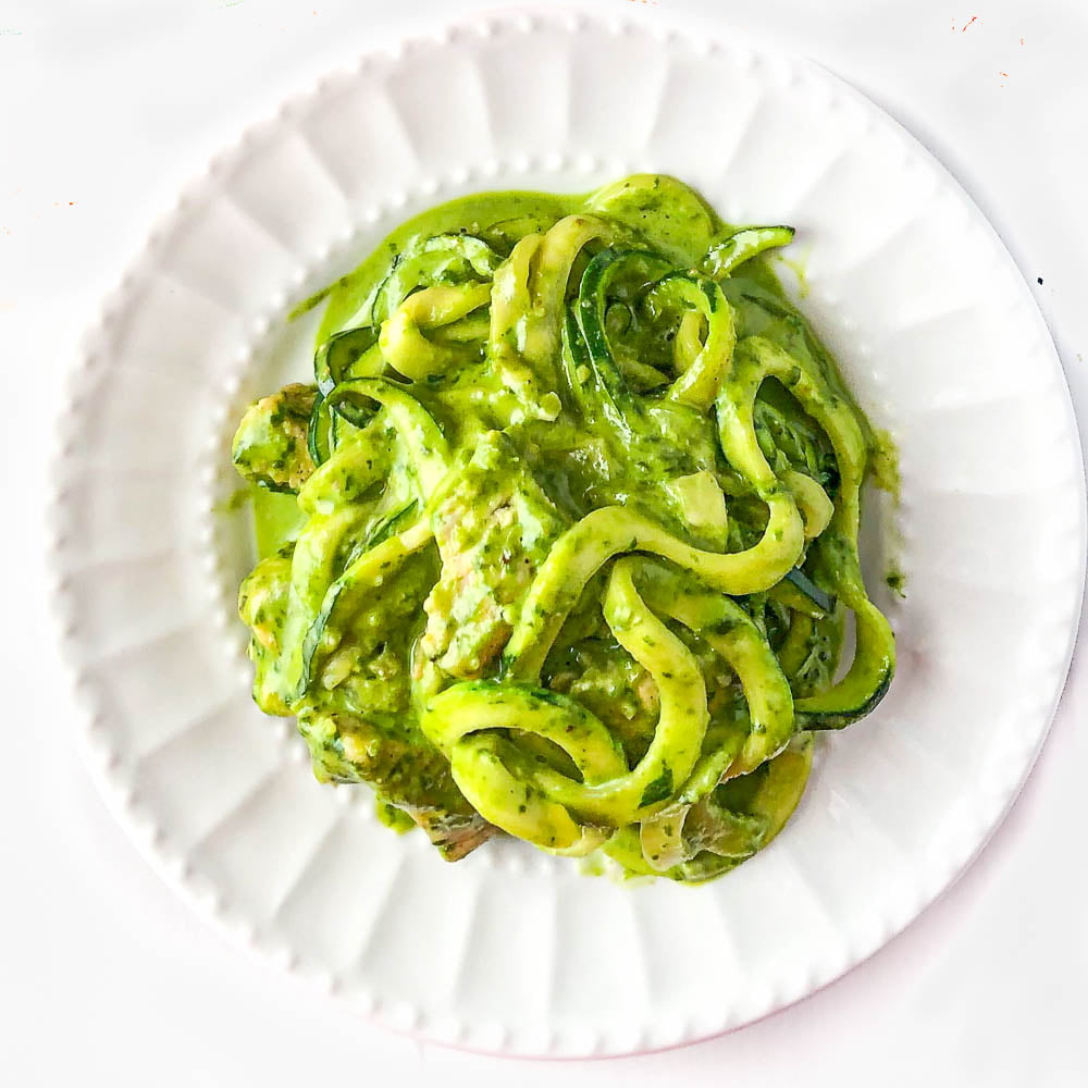 white plate with zucchini noodles and chicken in a creamy pesto sauce 