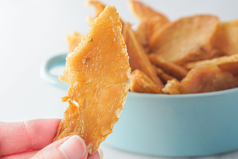 fingers holding a piece of homemade chicken dog jerky treats