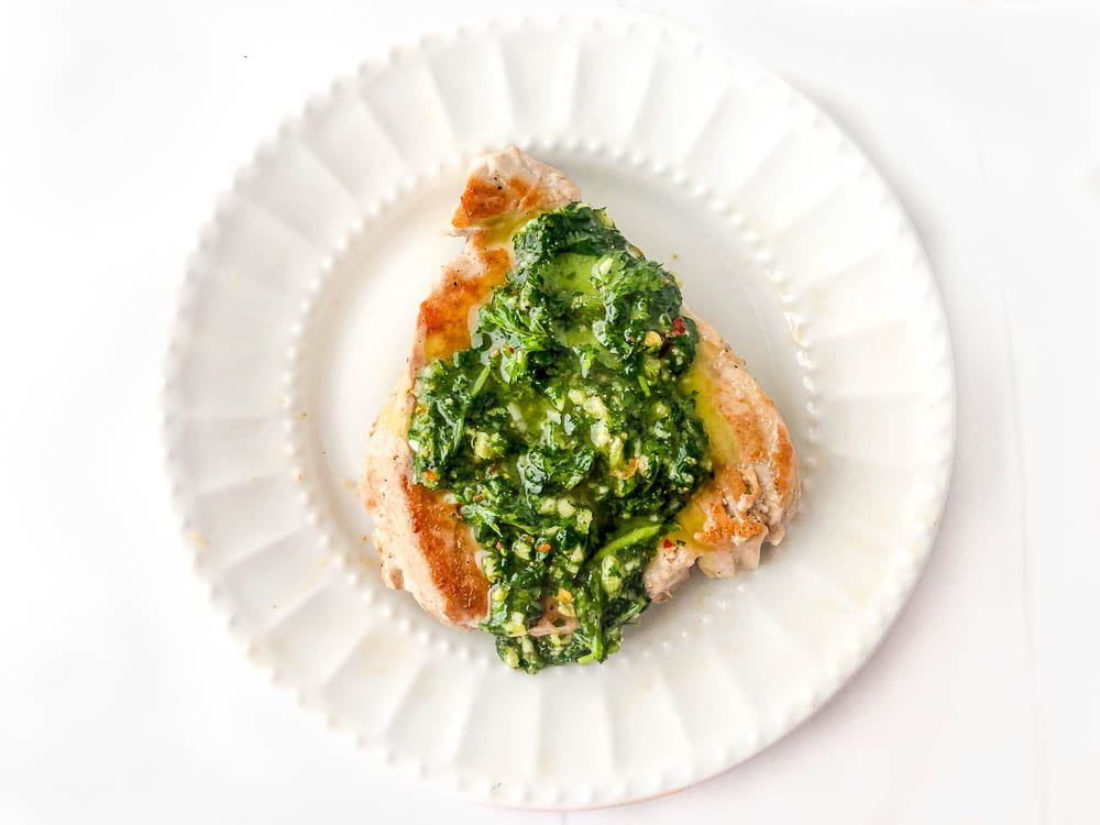 a piece of tuna steak on a white plate with cilantro green sauce on top