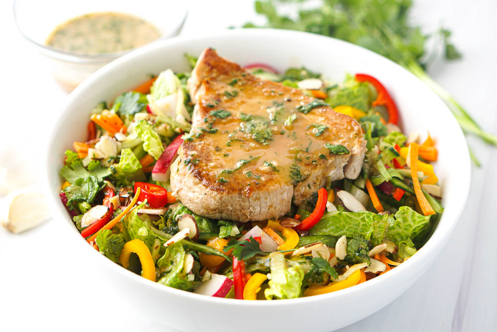 white bowl with colorful salad and topped with a tuna steak and Asian salad dressing