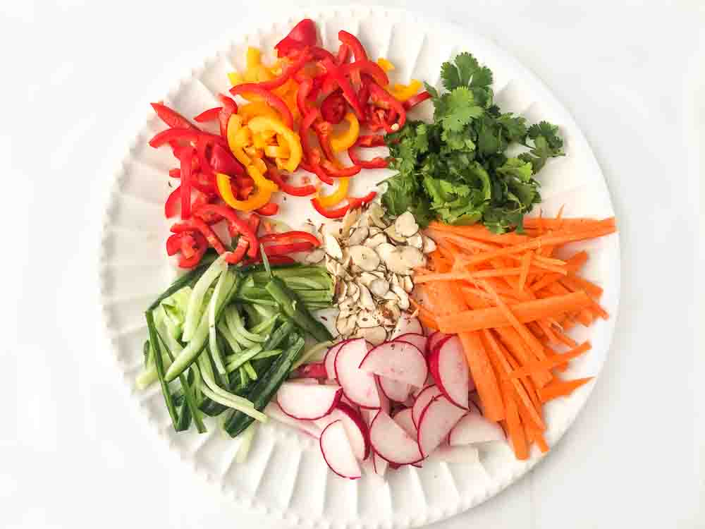 white plate with cutup colorful vegetables for Asian salad