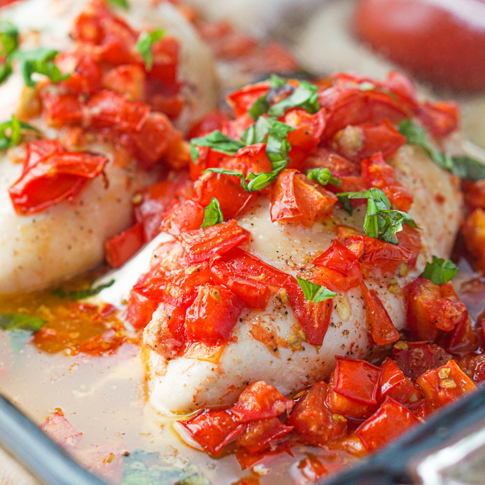 closeup of baking dish with chicken and chopped tomatoes