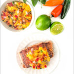 white plate with salmon topped with mango salsa and text
