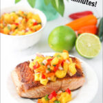 white plate with salmon topped with mango salsa and text