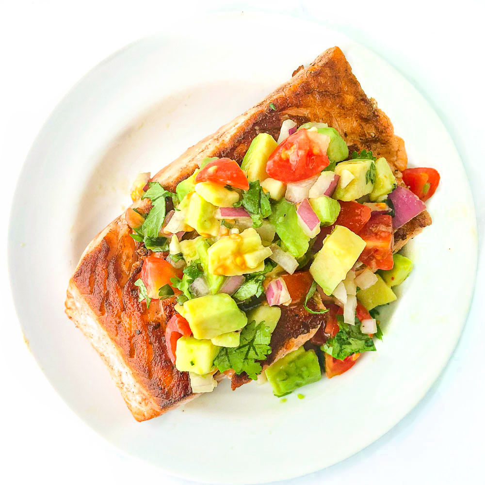 white plate with salmon topped with chunky avocado salsa