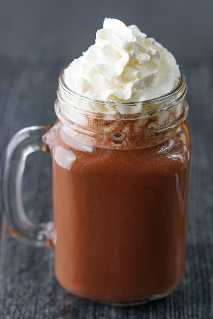 tall photo of hot cocoa in a mason jar glass with whipped cream