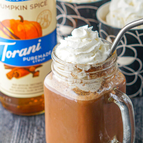 closeup of a glass jar cup with hot chocolate with whipped cream and silver straw