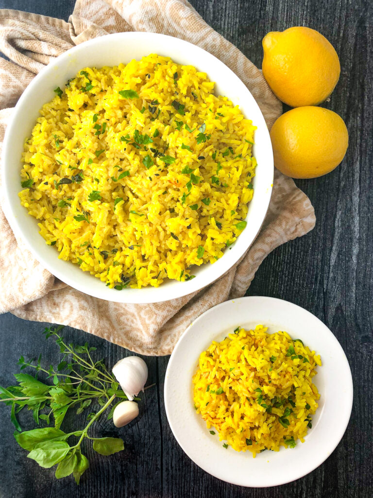 aerial view of a bowl and plate with lemon herb rice and fresh lemons and herbs and garlic