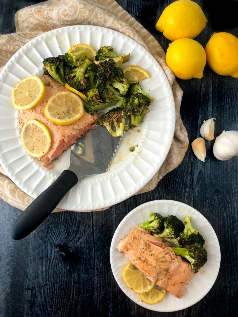 large and small white plates with salmon, broccoli and fresh lemons and garlic cloves