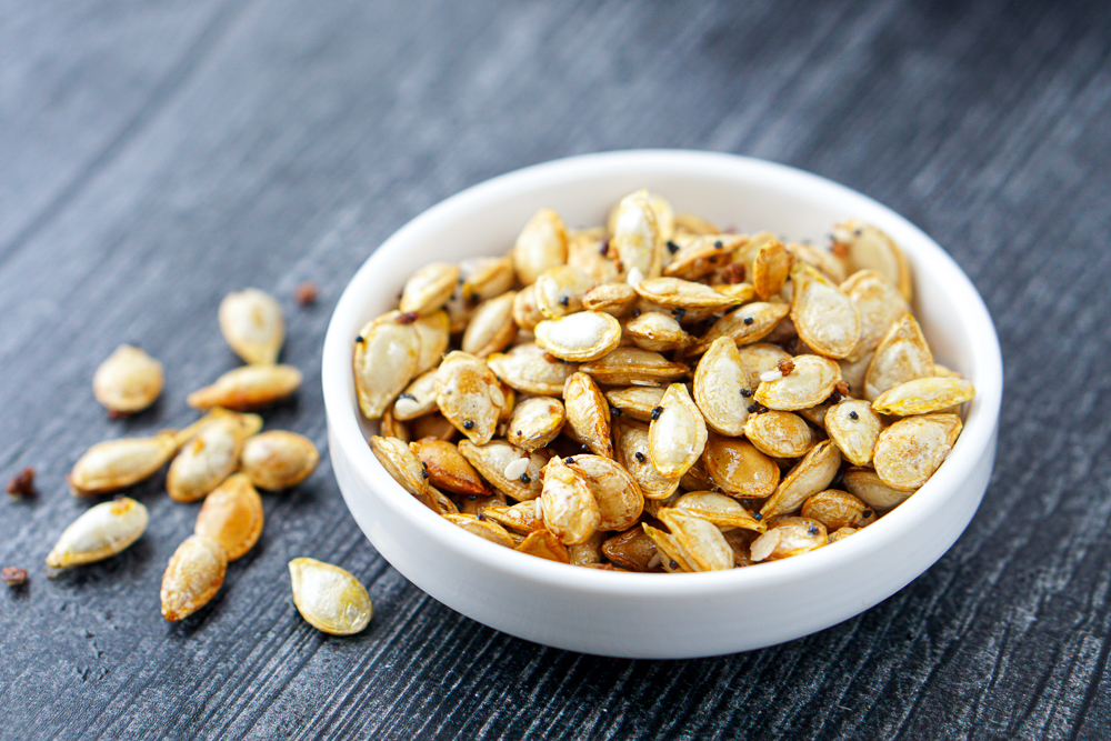 closeup of a bowl of roasted seeds with a few scattered on the table