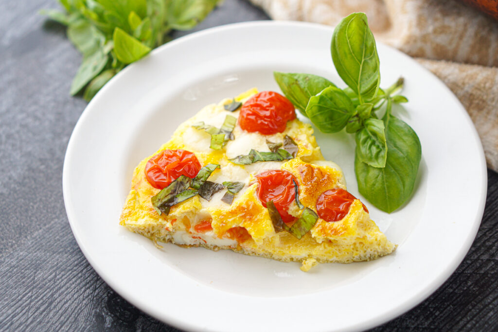 closeup of a slice of caprese omelet and some fresh basil leaves