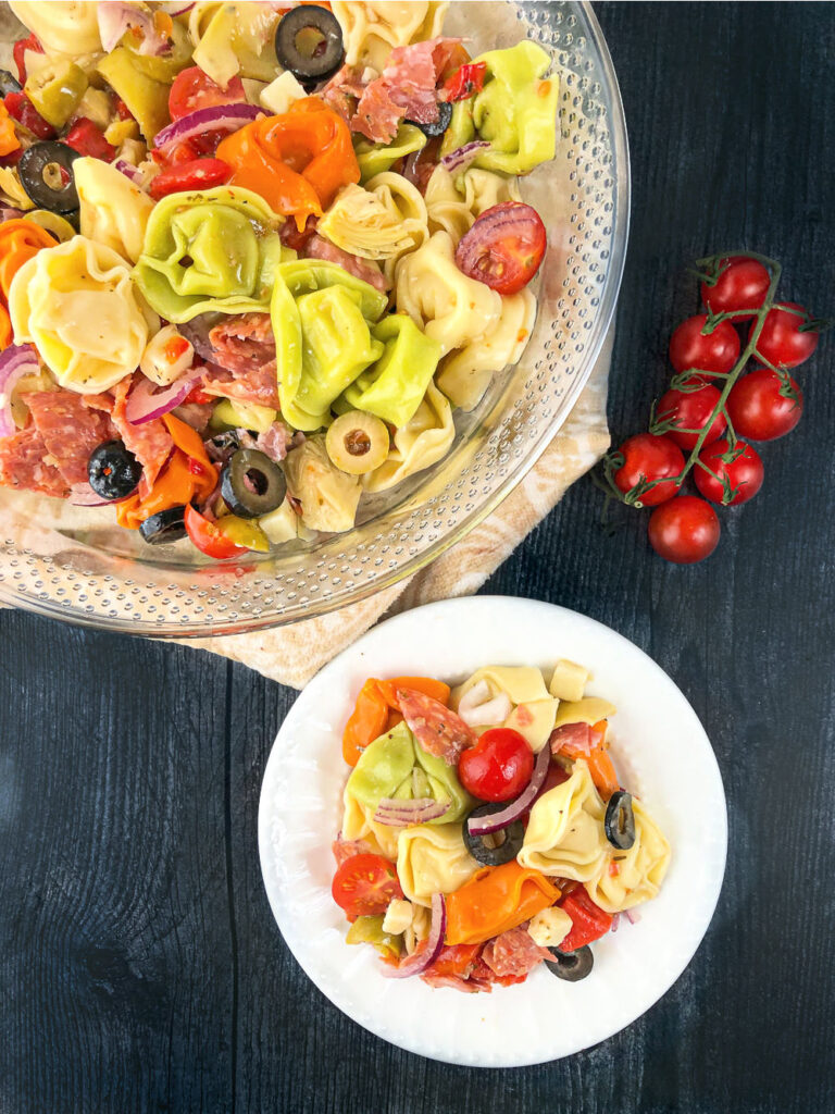 glass bowl and white plate with Italian pasta salad and fresh tomatoes