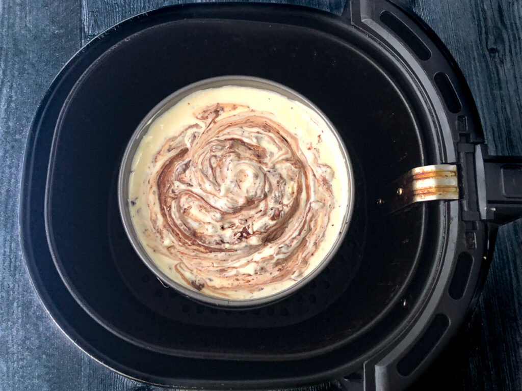 air fryer basket with unbaked cheesecake in a springform pan