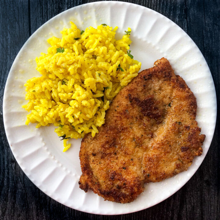 white plate with a breaded chicken cutlet and yellow rice