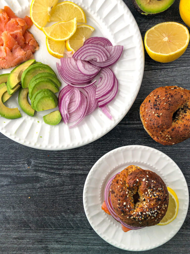 aerial view of a plate of sandwich toppings - smoked salmon, avocado, lemon wedges, red onions and everything bagels