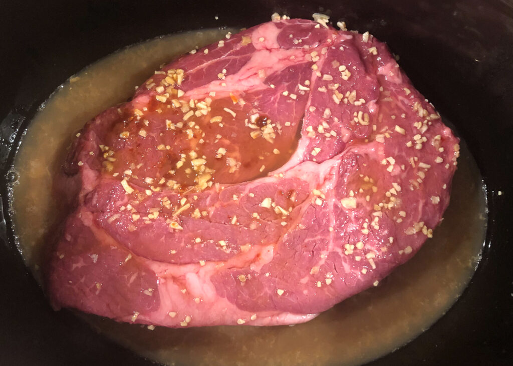 crockpot with a raw chuck roast and seasonings