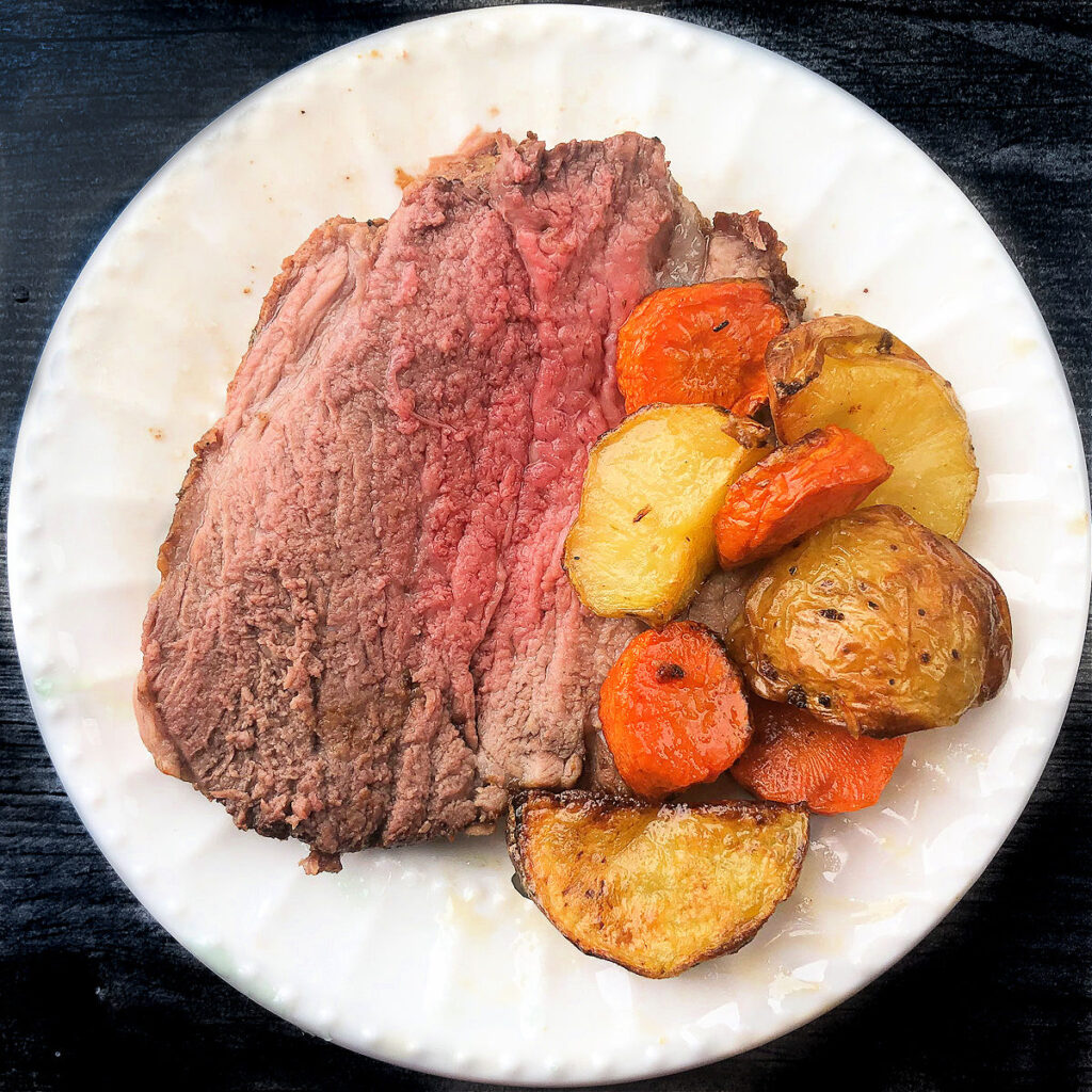 white plate with a slice of air fryer lamb, potatoes and carrots