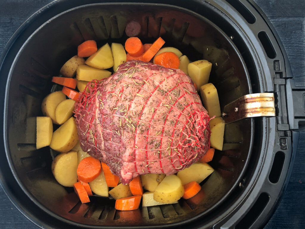 air fryer basket with lamb roast and vegetables ready to cook