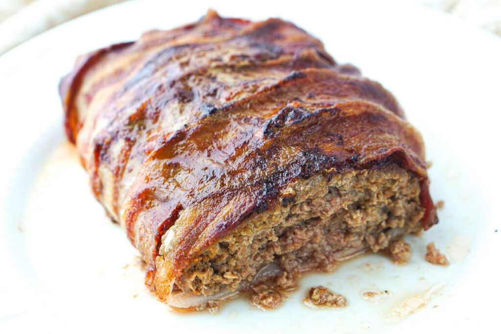 closeup of a loaf of meatloaf that's covered in bacon and has a piece cut off.