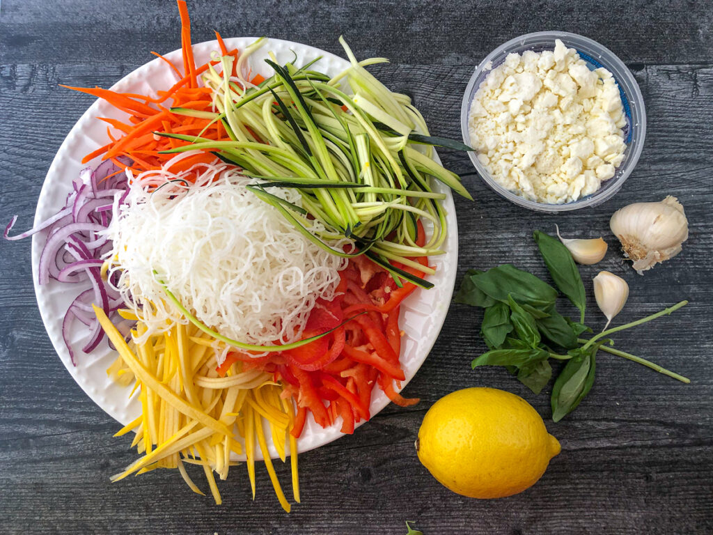 ingredients for this veggie noodle recipe - colorful vegetable noodles, feta cheese, fresh lemon, fresh basil and garlic cloves