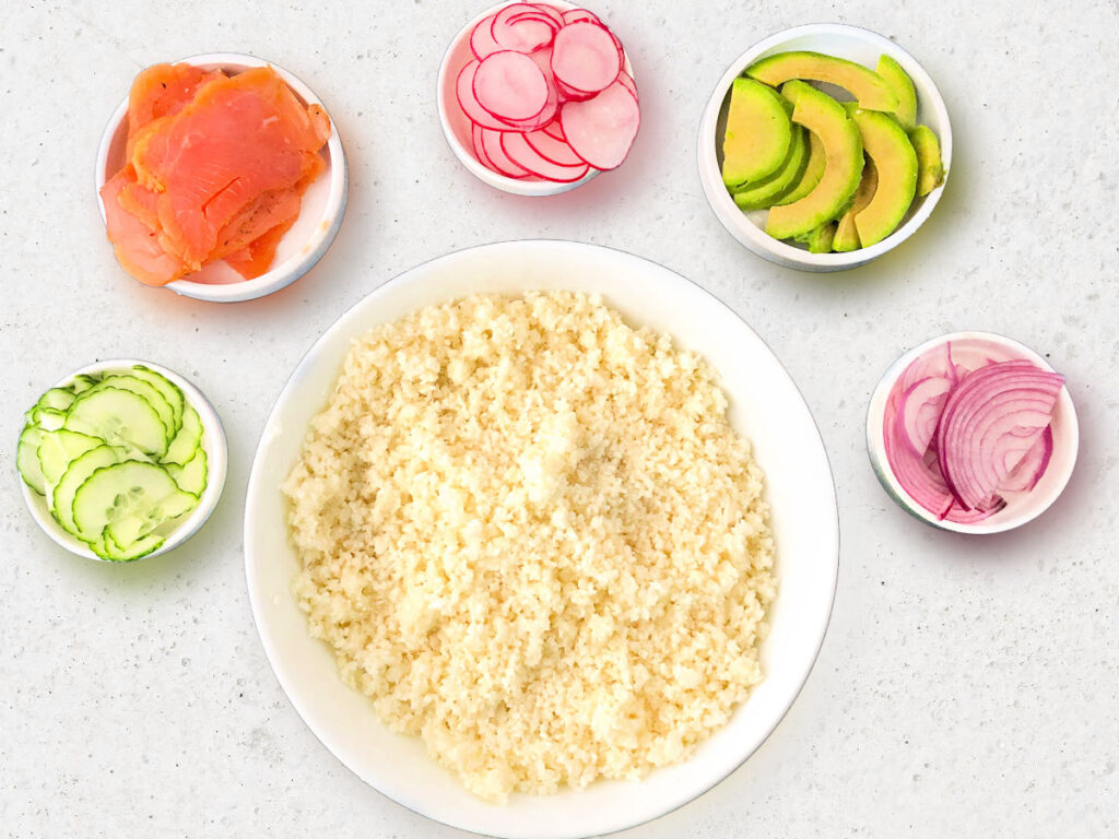 Recipe ingredients for the bowl - cauliflower rice, avocado slices, radish slices, onion slices, cucumber slices.