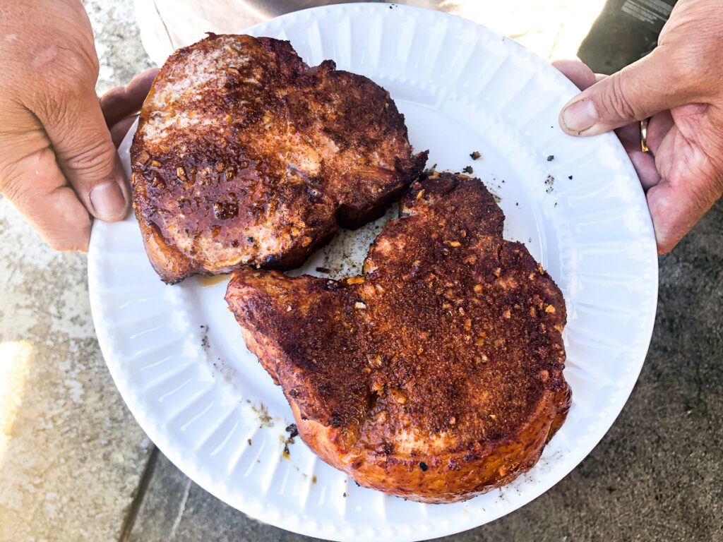 hands holding a plate with 2 pork chops fresh out of the smoker