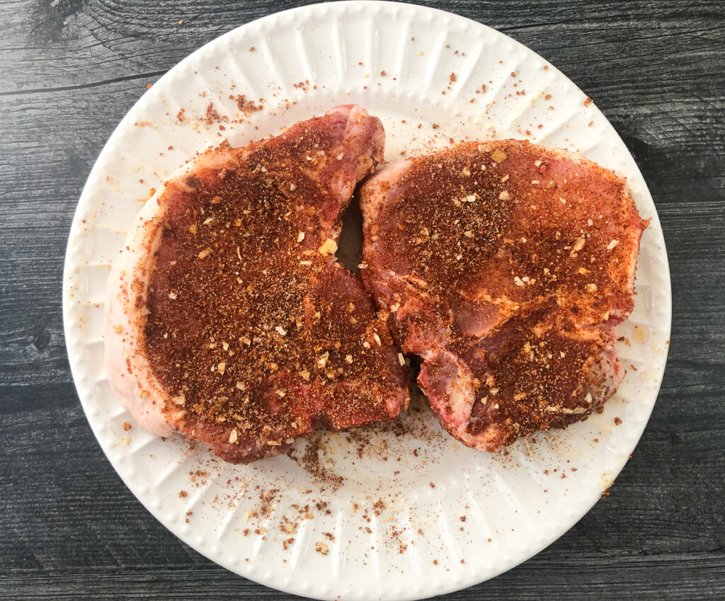 white plate with 2 raw chops rubbed with spices