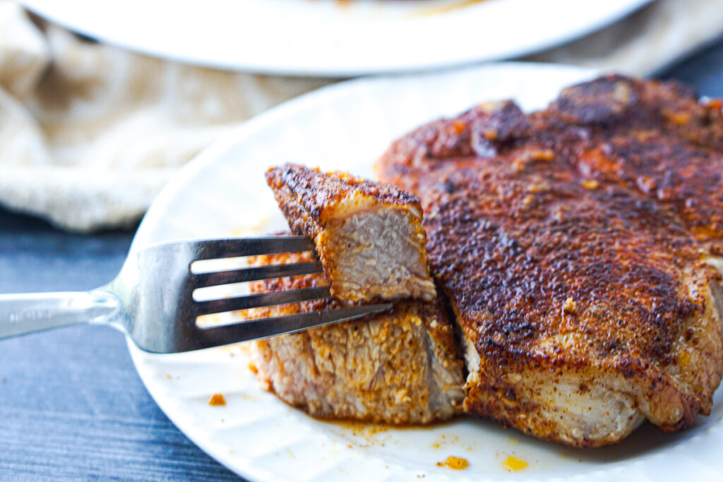 white plate with a pork chops with a bite taken out on a fork