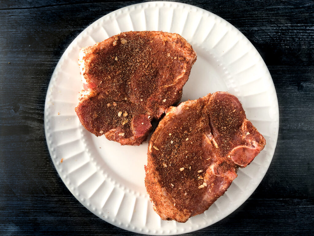 white plate with raw chops rubbed in seasonings
