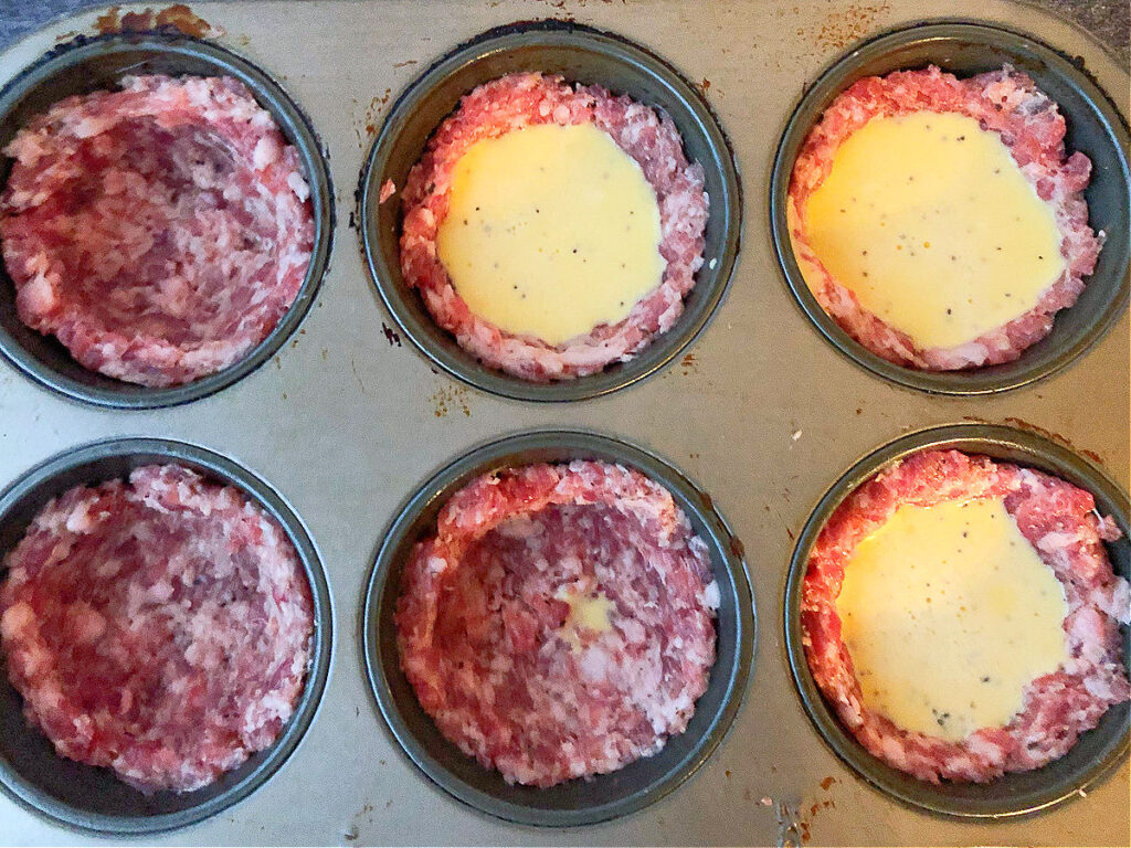 muffin tin with raw sausage formed into a cup white egg poured in the middle