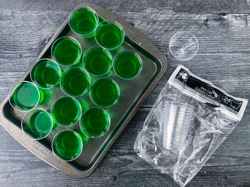 baking tray with freshly poured lime jello shots and a bag of plastic shot glasses