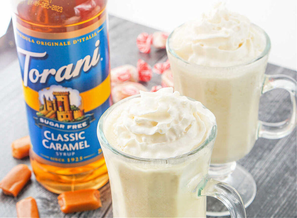 2 clear glasses with low carb milkshakes with a bottle of caramel syrup