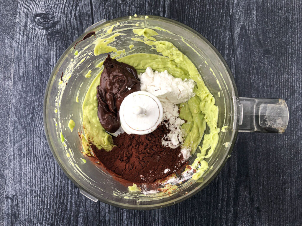 food processor bowl with avocado, swerve sweetener, cocoa powder and melted chocolates