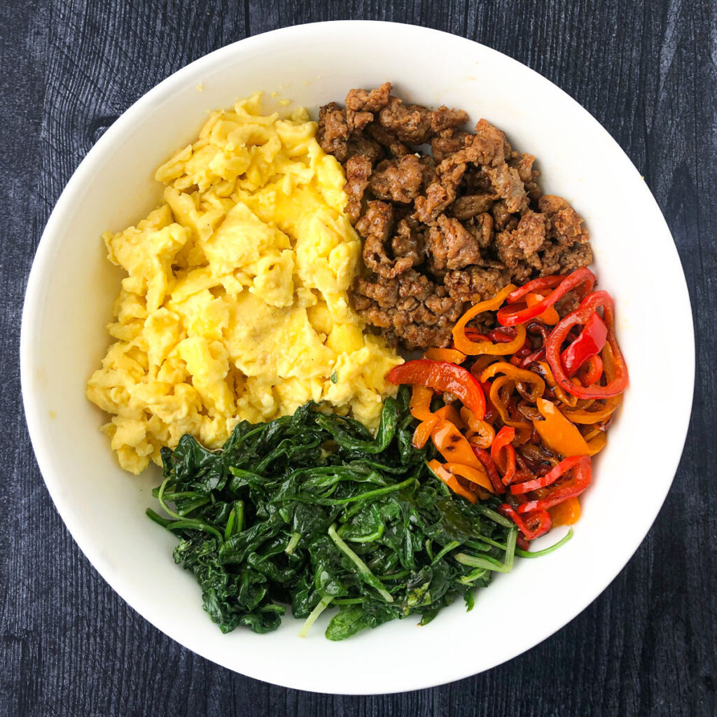 white bowl with eggs, sausage, salted peppers and spinach
