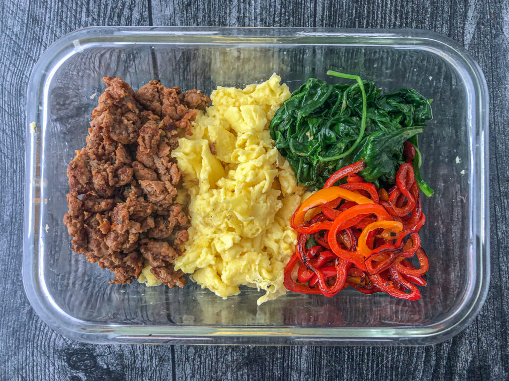 glass storage container with turkey sausage, scrambled eggs, sautéed spinach and peppers