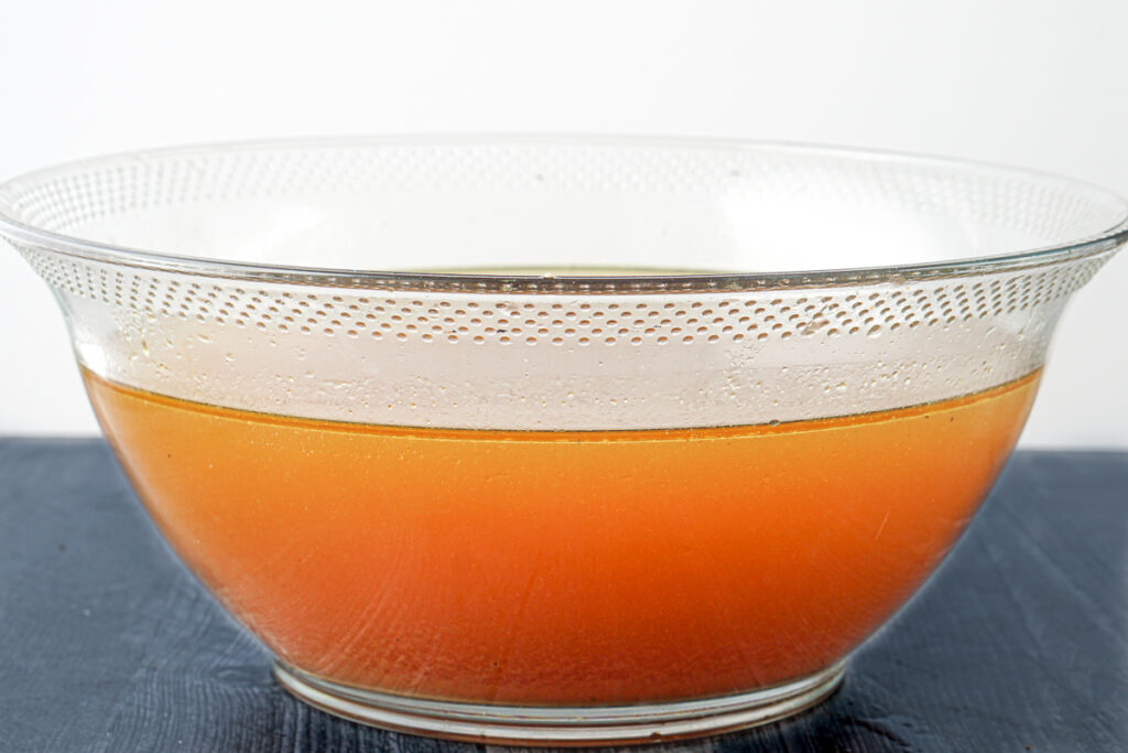 strained homemade chicken bone broth in a large glass bowl