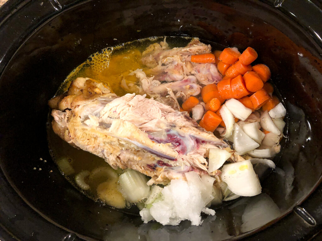 crock pot filled with leftover chicken bones, vegetables and seasonings