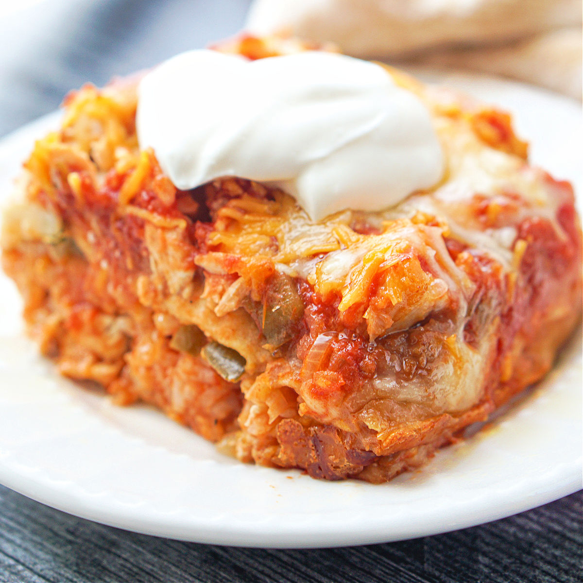 closeup of a piece of chicken burrito casserole with sour cream on top