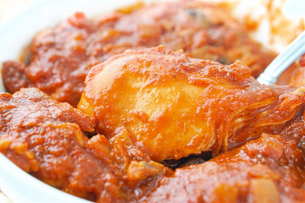 closeup of a spoon holding a piece of tender slow cooker chicken in sauce