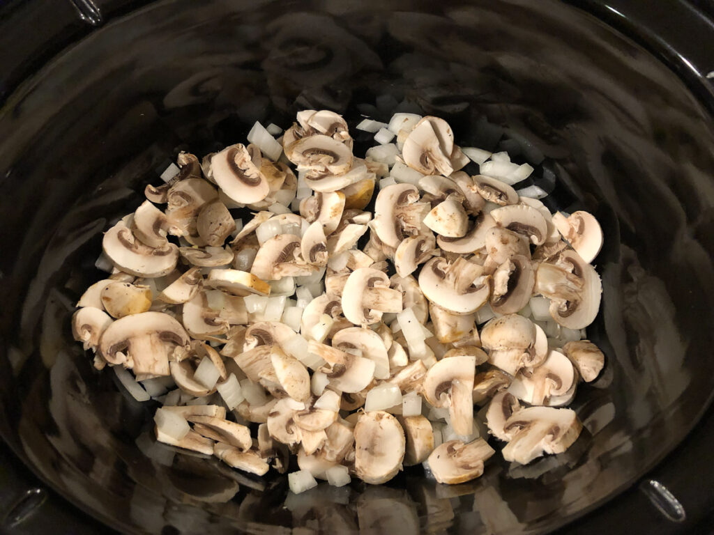 crock pot with sliced mushrooms and chopped onions