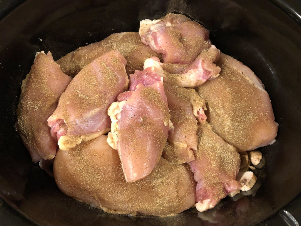 slow cooker crock with raw chicken rubbed with spice blend