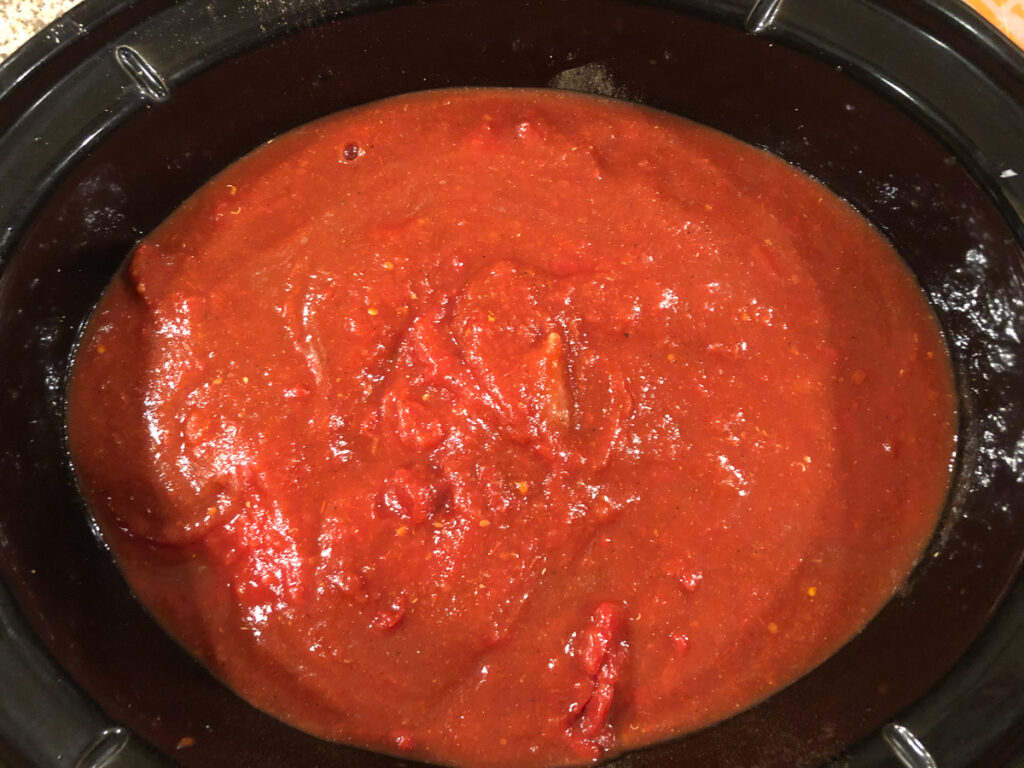 crock of slow cooker with sauce and seasonings