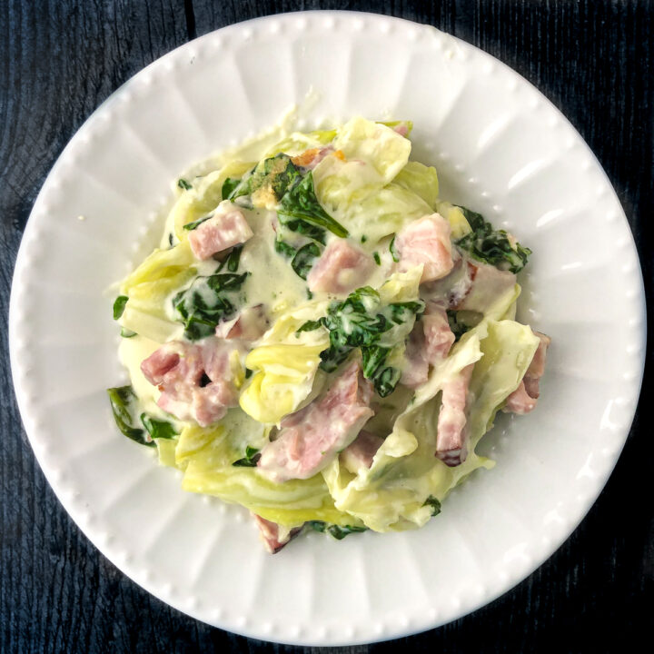 white plate with creamy cabbage noodles with ham and spinach