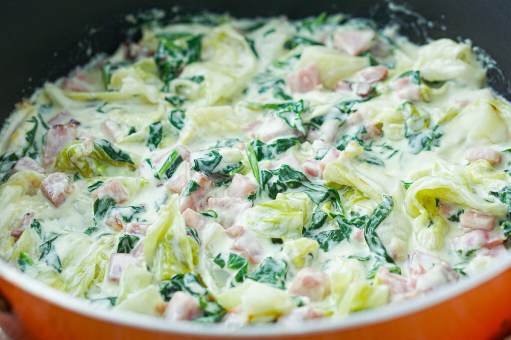 closeup of a pan with cabbage noodles and creamy parmesan sauce and ham