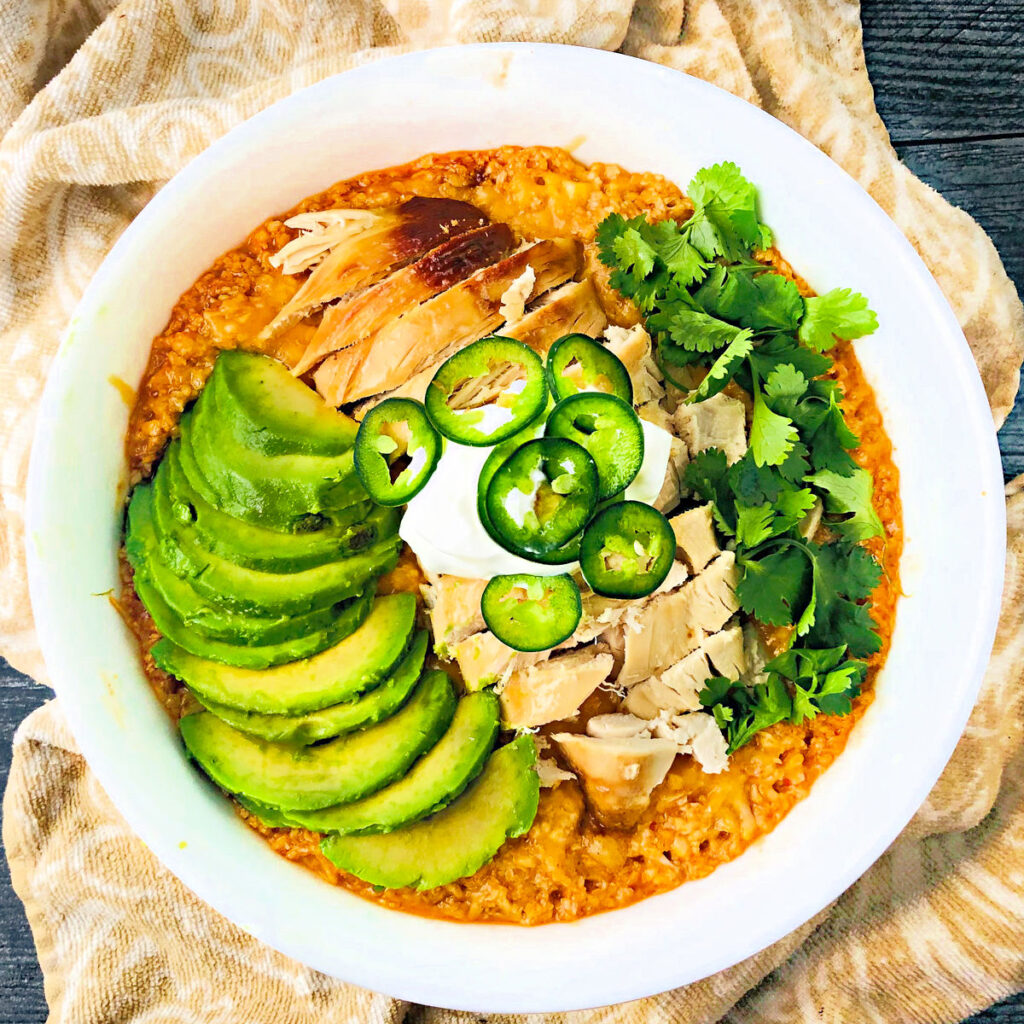 big white bowl with keto chicken enchilada bowl of cauliflower rice, chicken, avocado, sour cream, jalapenos and cilantro